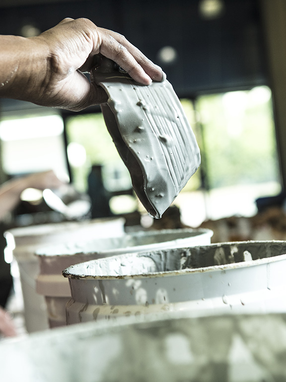 hand holding a ceramic dish over a paint bucket