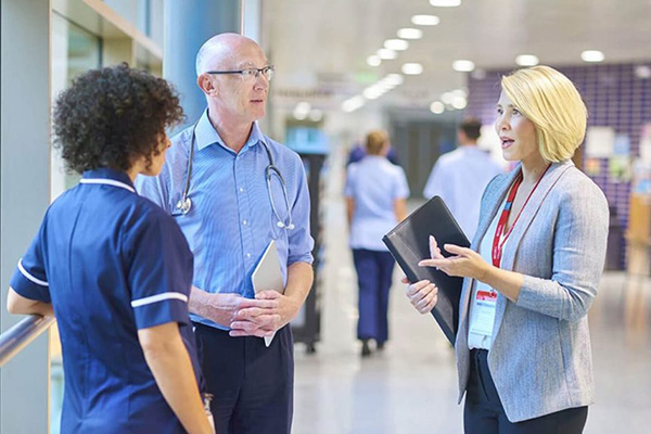 Three healthcare professionals have a conversation in a hospital lobby.