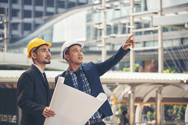 Two civil engineers in professional attire wearing hardhats discussing blueprints.