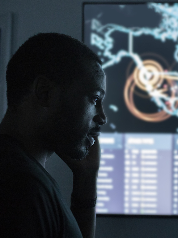 A cybersecurity student in front of a large world map and status display.