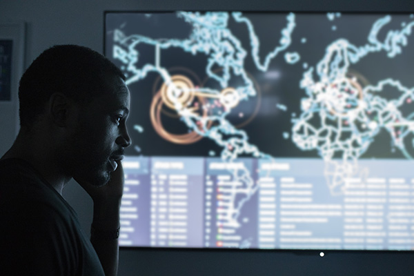 cybersecurity student in front of a large cyber threat dashboard