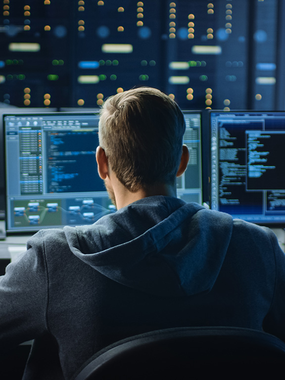 cybersecurity worker looking at three monitors in a server room