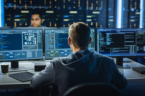 cybersecurity worker looking at three monitors in a server room