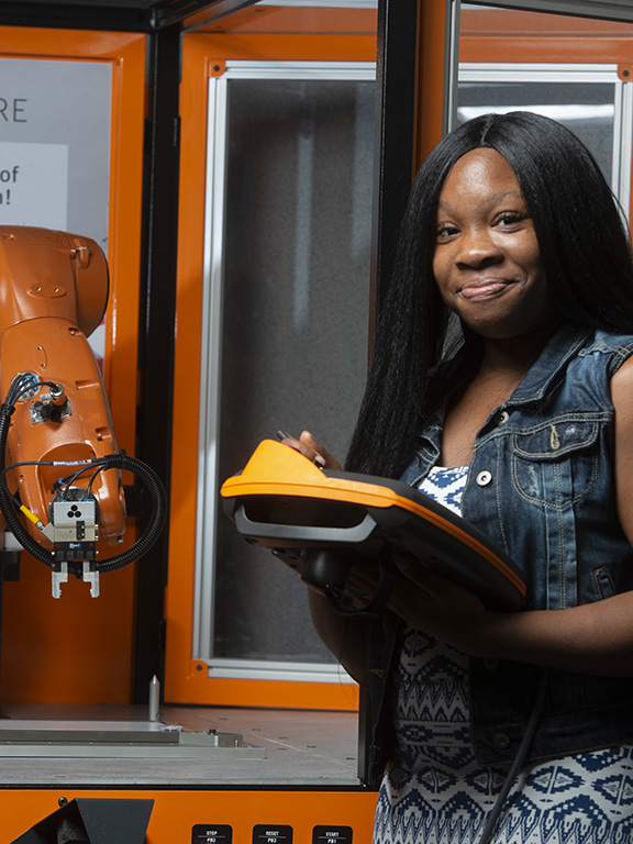 Engineering student using a tablet to control a robotic arm.