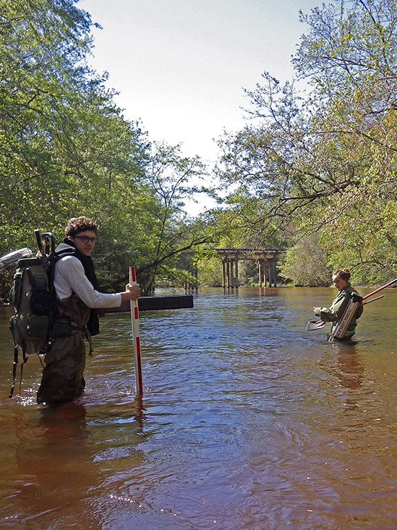 Two UWF students wading through a local river taking water samples.