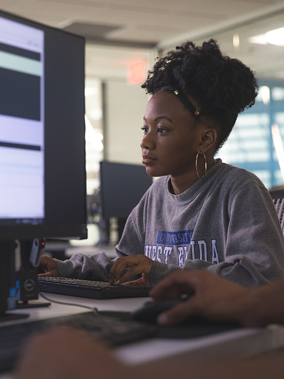 A student using a computer with a screen of a different computer present in the foreground.