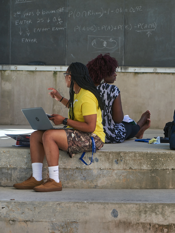 Two students sitting and studying outside in front of a chalk board.