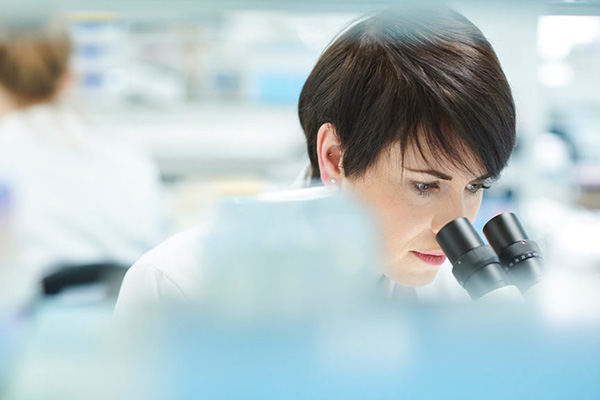 Lab worker looking through a microscope in a lab setting.