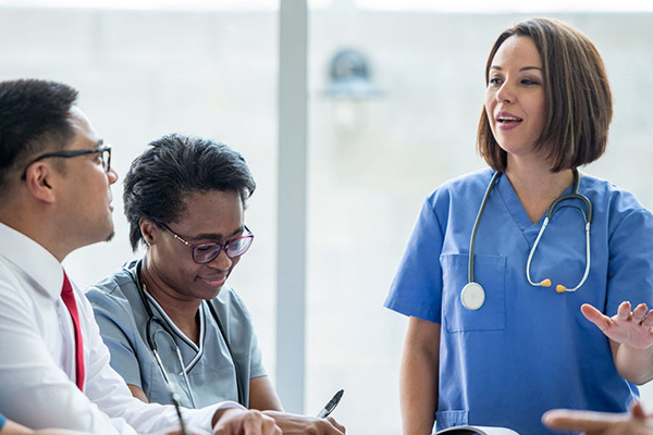 a nurse in scrubs leads a training session for two people sitting at a desk