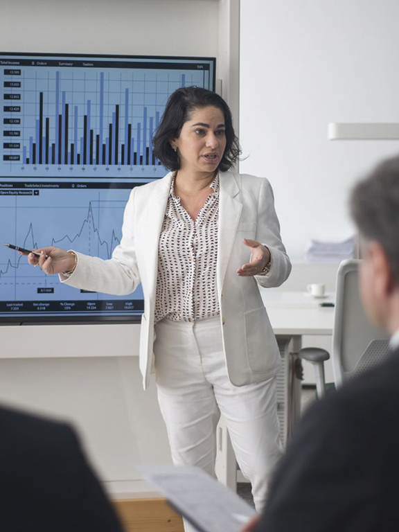 Business professional presenting data displayed on conference room screen.