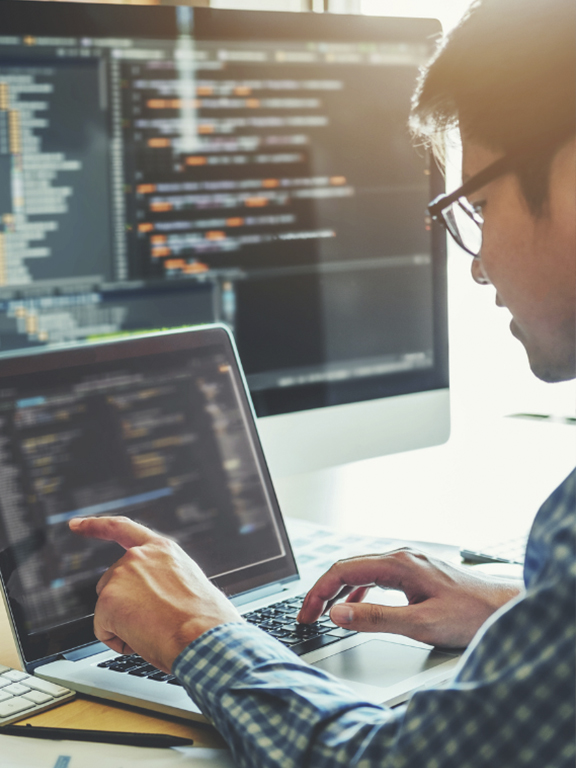 Cybersecurity expert working on a computer with multiple screens showing software code.