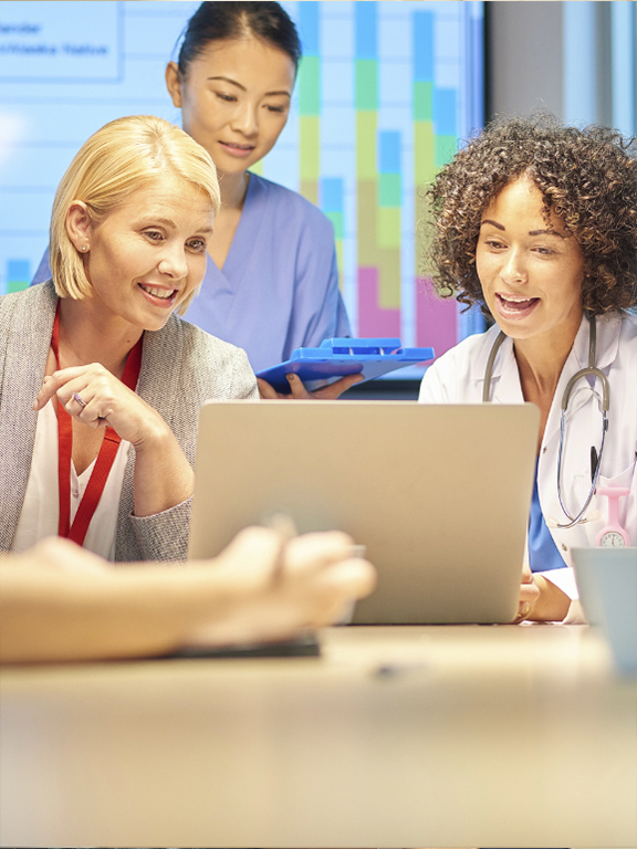 Healthcare professionals meeting and conversing around a laptop.