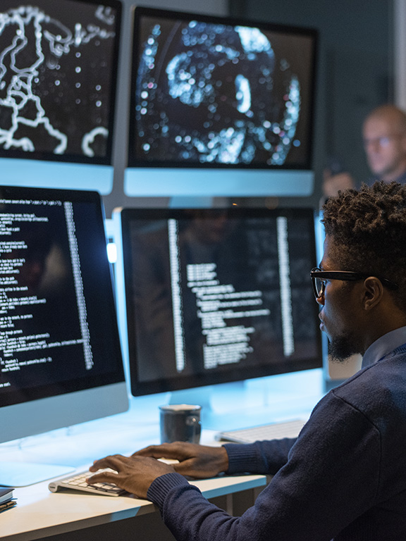 Information security manager while sitting in front of computer monitors and looking at screen of one of them