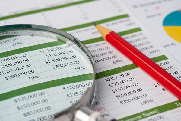 Magnifying glass and pencil on top of a sheet of paper with a finance spreadsheet.