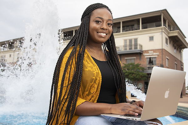 Student using a laptop while sitting in front of a water fountain.