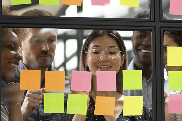 Five individuals collaborating using post it notes on a see-through board to share ideas.