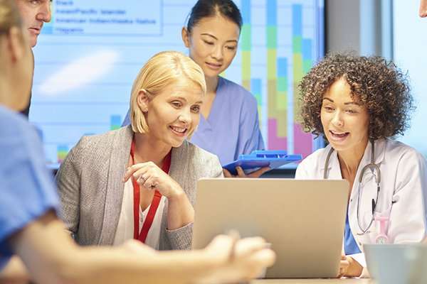 Healthcare professionals meeting and conversing around a laptop.