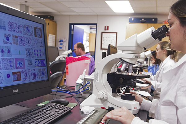 Students in lab coats using microscopes in a classroom setting.