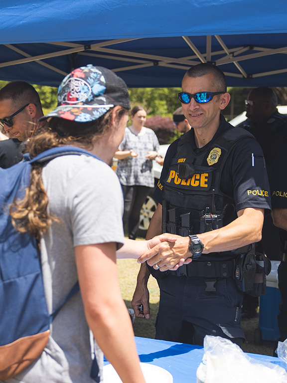 A police officer in uniform shaking hands with a student during an outdoor event.