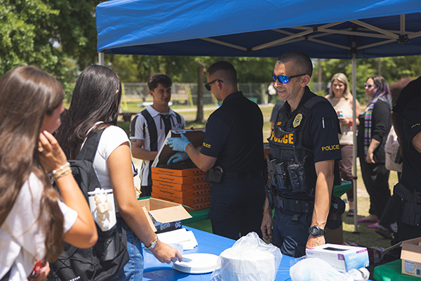 Two police officers in uniform serving students pizza during an outdoor event.