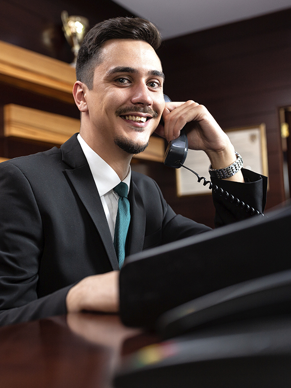Hotel manager in professional attire speaking on a landline phone.