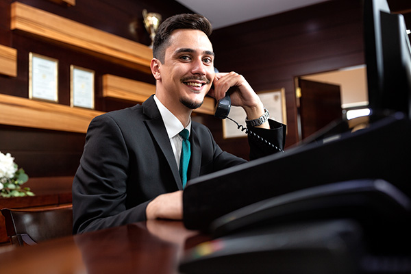 Hotel manager in professional attire speaking on a landline phone.