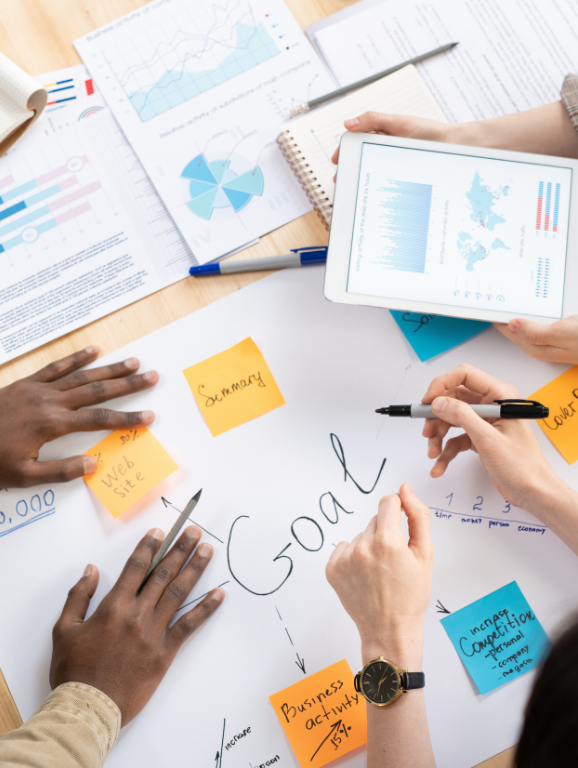 Four design professionals sitting in a circle on the floor, collaborating on a project with notes, papers, and a laptop spread out in front of them.