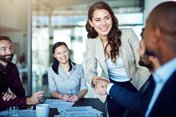 two people shaking hands in front of two more people at a business meeting