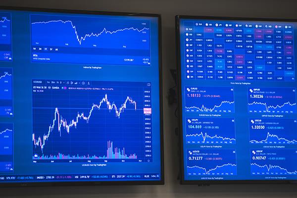 Two monitors displaying various stock market and financial graphs.