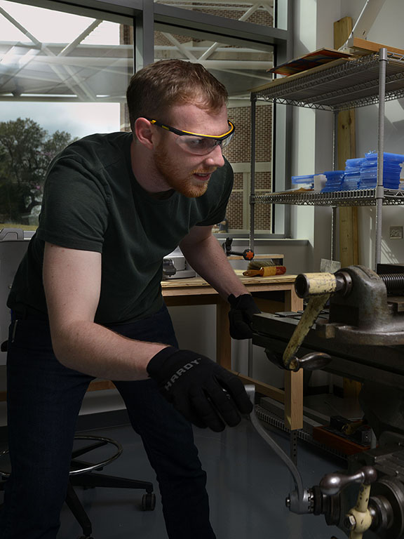 Mechanical engineering student wearing safety glasses and gloves while using a mill machine in a fabrication lab.