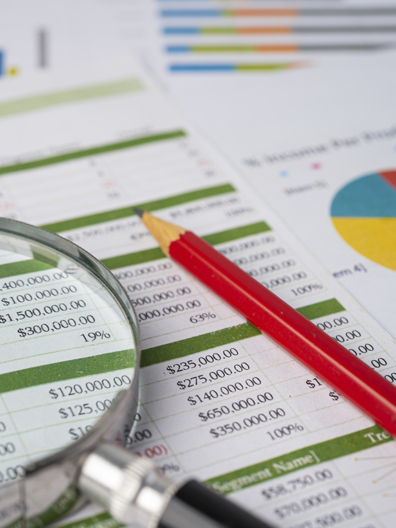 Magnifying glass with pencil on finance spreadsheet table and graph paper