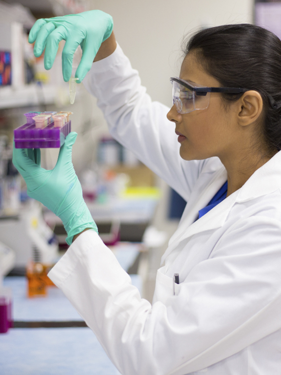 Public health worker in the lab wearing eye protection and lab coat.