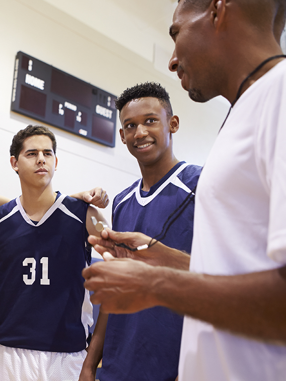Close up of a high school basketball team talking to a coach with a scoreboard in the background.