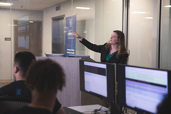 Professor teaching a class of students in a cybersecurity classroom lab.