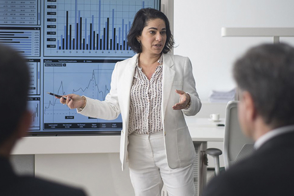 Business professional presenting data displayed on conference room screen.