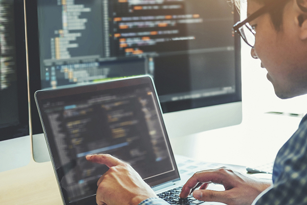 Cybersecurity expert working on a computer with multiple screens showing software code.