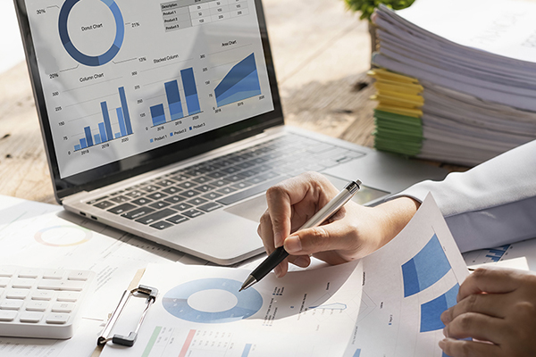 Person holding a pen while working on a data project while using a laptop that also displays data charts and graphs.