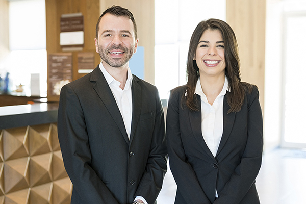 Two hospitality professionals in professional attire standing in a hotel lobby.