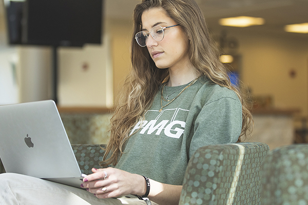 Student using a laptop while sitting on a couch in a school building lobby.