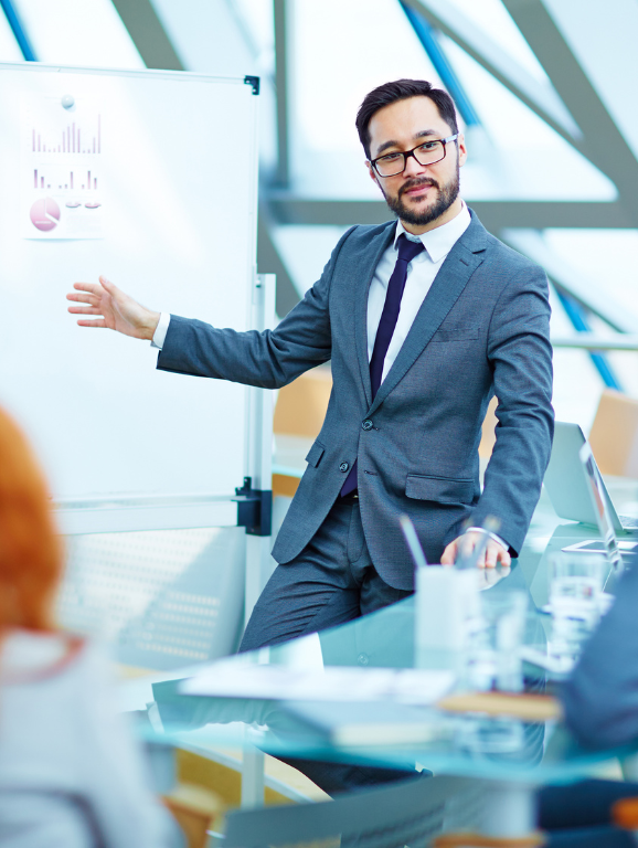 Business professional giving data presentation in front of a board displaying print outs of charts and graphs.