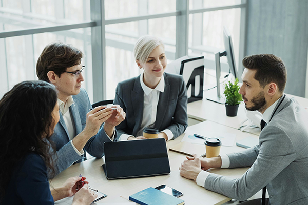 Four finance professionals in professional attired seated at indoor desk station collaborating.