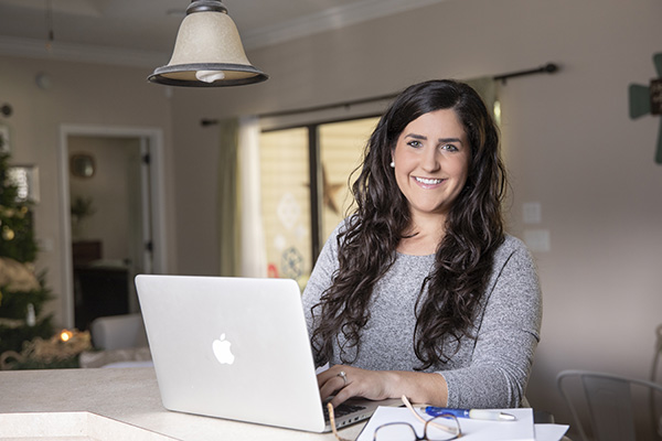 student typing on a macbook laptop at a desk at home