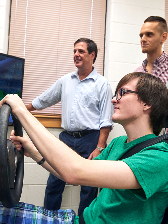 Psychology student using a driving simulator as a graduate student and professor record the results.