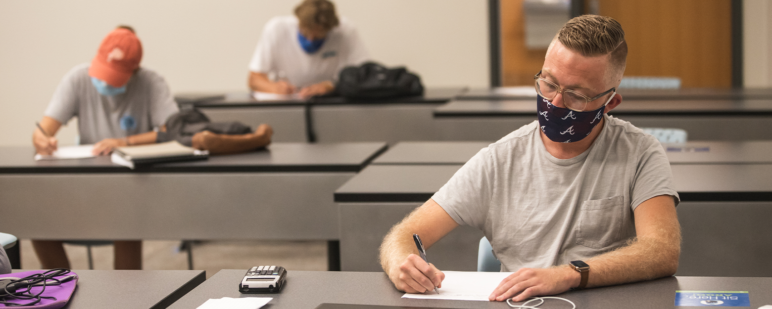 socially distanced business students writing at desks in class