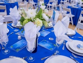 An elegant table setting with blue table covers and white plates and napkins and a live floral bouquet in the center of the table