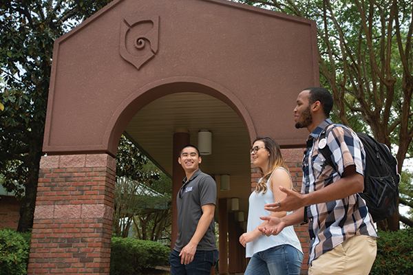 Three students walking by a brick archway entrance with a nautilus shell artwork imprinted on the arch.