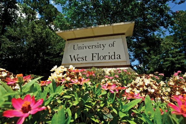 University of West Florida campus entrance monument sign with flowers in the foreground and trees in the background.