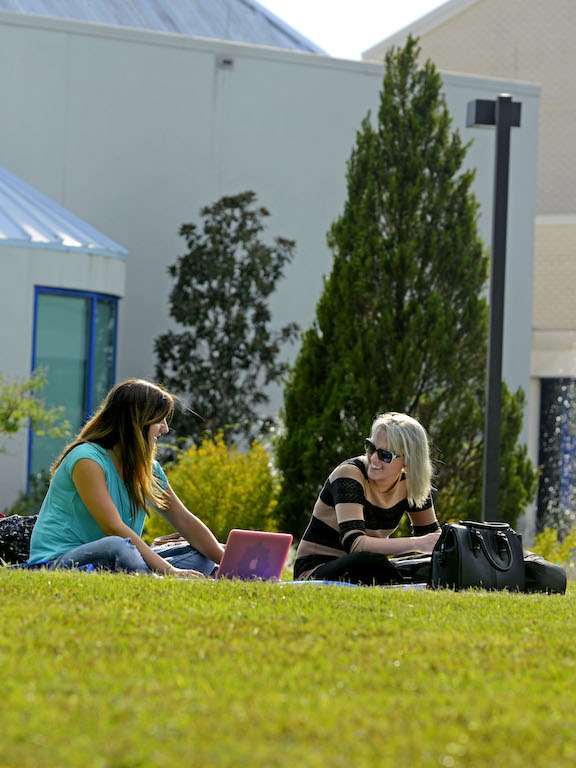 two female students studying outdoors in the grass on campus