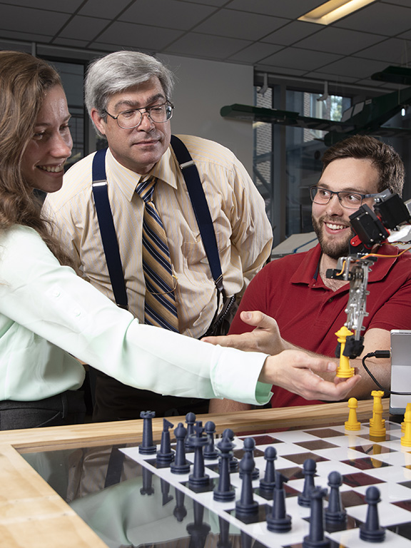 UWF professor and two students working on a chess board mechanical and electrical engineering project.