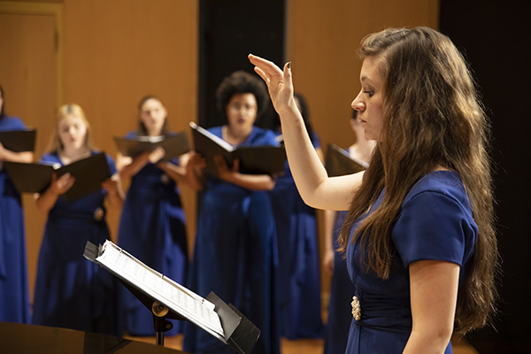 a choir conductor leads a chorus in the background